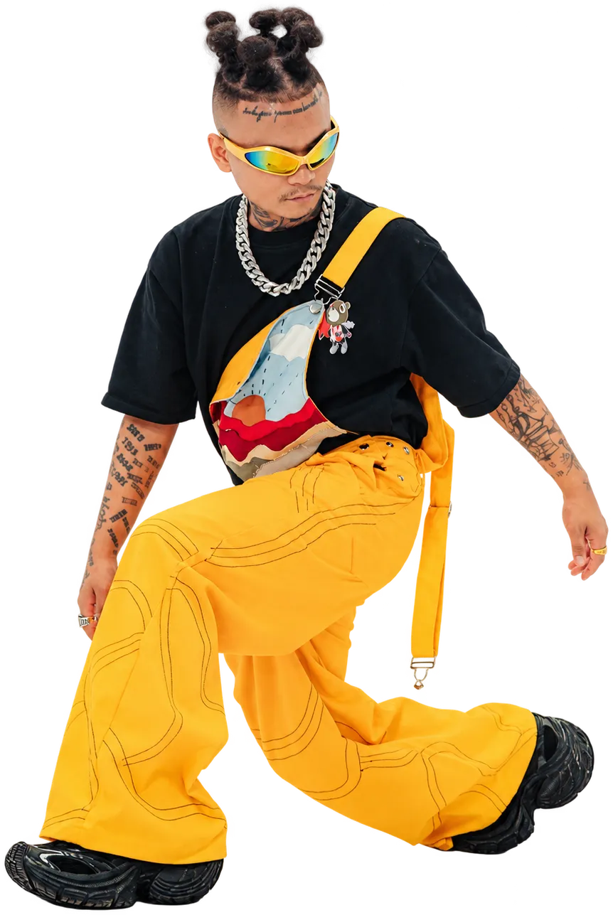 ST MAN seated in wraparound shades, a chain and wide yellow trousers, one leg drawn up